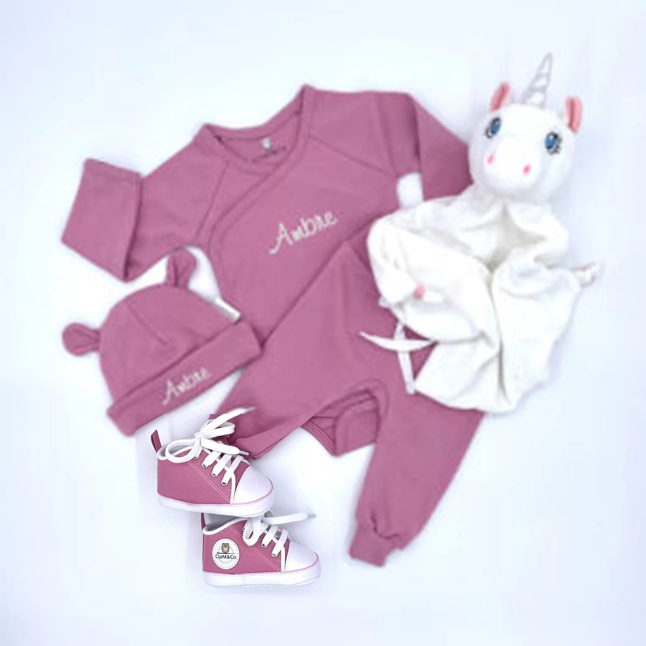 Coffret comprenant un body, un pantalon, des chaussures, un bonnet et un doudou rose.